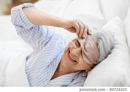 senior woman with eye sleeping mask in bed at home senior woman with eye sleeping mask in bed at home 80728203