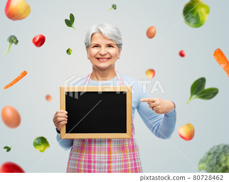 smiling senior woman in apron with chalkboard 80728462