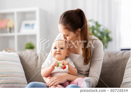 mother kissing baby with teething toy at home mother kissing baby with teething toy at home 80728834