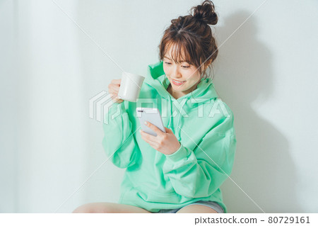 一個女人在房間裡喝咖啡時看著她的智能手機 一個女人在房間裡喝咖啡時看著她的智能手機 80729161