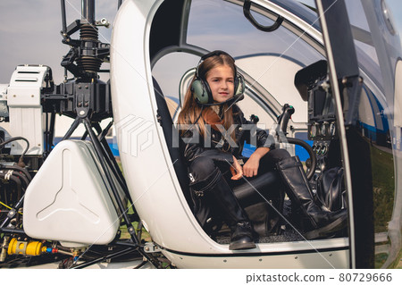 Confident tween girl in pilot headset sitting in helicopter cockpit 80729666