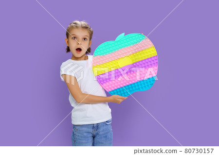 Surprised kid holding huge apple anti stress bubble. motor skills. pop it fun. child holding color popit fidget 80730157