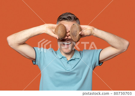 Man holding two coconuts at eye level 80730703