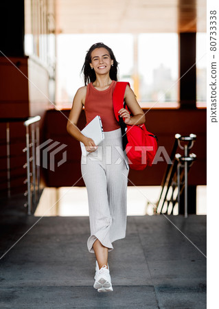 A smiling student with a backpack and a laptop climbs the stairs at the college, hurries to lectures A smiling student with a backpack and a laptop climbs the stairs at the college, hurries to lectures 80733338