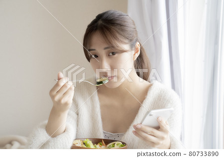 A woman eating a salad and a smartphone A woman eating a salad and a smartphone 80733890