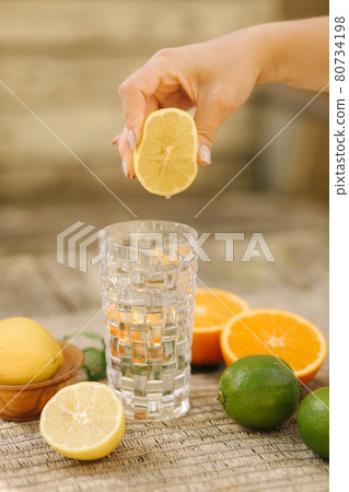 Home made healthy vitamin-fortified water. Woman squeezes lemon juice in water 80734198