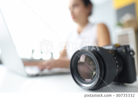Black professional camera lying on background of woman laptop closeup Black professional camera lying on background of woman laptop closeup 80735332