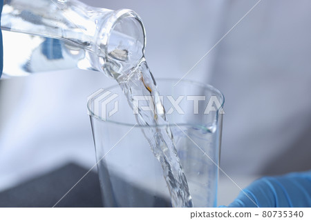Scientist chemist pouring water from transparent bottle into flask in laboratory closeup 80735340