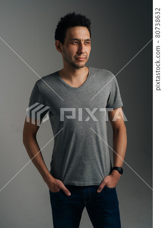 Vertical portrait of confident young man in gray T-shirt standing with with hands in pockets on dark isolated background. Vertical portrait of confident young man in gray T-shirt standing with with hands in pockets on dark isolated background. 80738632