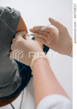 Close-up vertical shot of female doctor in safety medical latex gloves giving injection vaccine dose in shoulder. Close-up vertical shot of female doctor in safety medical latex gloves giving injection vaccine dose in shoulder. 80738637
