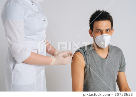 Studio shot of young man in face mask giving injection vaccine against coronavirus during vaccination on isolated white background. Studio shot of young man in face mask giving injection vaccine against coronavirus during vaccination on isolated white background. 80738638