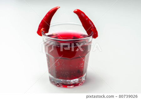 Drink shot prepared with vodka, grenadine and lemon juice decorated with bird eye chillies in the shape of horns 80739026