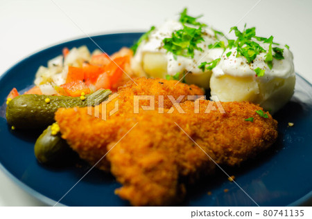 Breaded and herbed chicken breast fillet served with mashed potatoes, tomato salad with onions and gherkin Breaded and herbed chicken breast fillet served with mashed potatoes, tomato salad with onions and gherkin 80741135