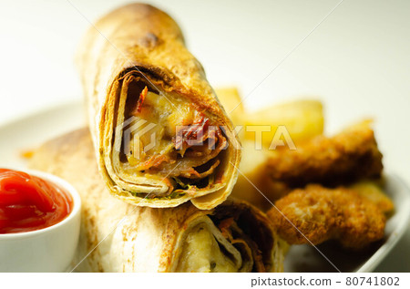 Tortilla wrap with chicken and beechwood smoked bacon served with chicken nuggets and chips on the white plate 80741802