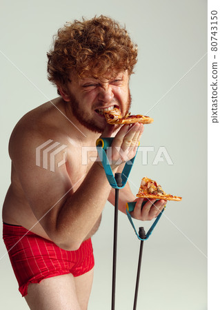 Cute red-headed man in red swimming shorts posing isolated on gray studio background. Concept of sport, humor and body positive. Cute red-headed man in red swimming shorts posing isolated on gray studio background. Concept of sport, humor and body positive. 80743150