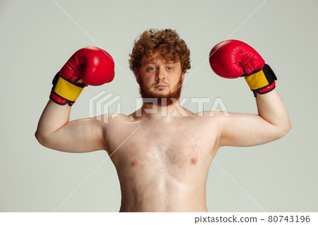 Funny red-headed man in blue boxing shorts and gloves isolated on gray studio background. Concept of sport, humor and body positive. Funny red-headed man in blue boxing shorts and gloves isolated on gray studio background. Concept of sport, humor and body positive. 80743196