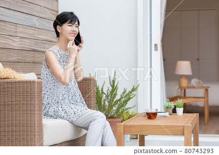 一位年輕女子在度假酒店的露台上用智能手機交談 80743293