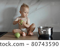 little boy sits on the kitchen countertop with green apples 80743590