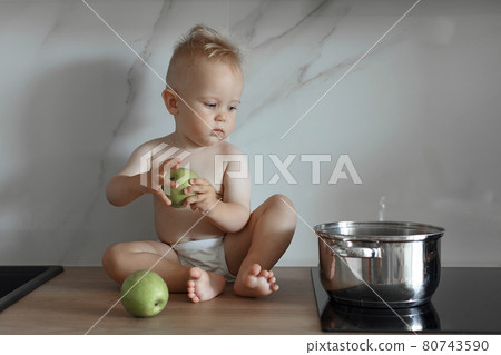 little boy sits on the kitchen countertop with green apples 80743590