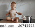 little boy in the kitchen is stirring soup in a saucepan 80743592