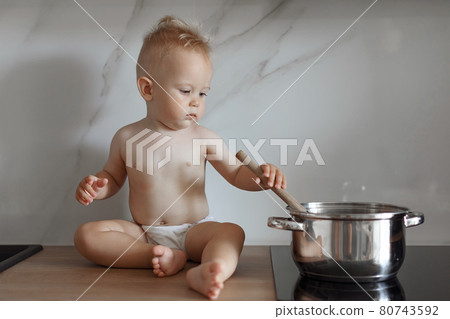 little boy in the kitchen is stirring soup in a saucepan 80743592