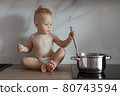 little boy in the kitchen is stirring soup in a saucepan 80743594