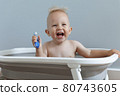 laughing small child rushes his teeth while sitting in the bathroom 80743605