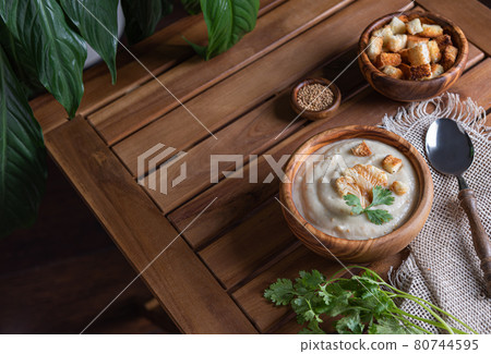 White cauliflower cream soup with croutons , spoon and herbs on brown table White cauliflower cream soup with croutons , spoon and herbs on brown table 80744595