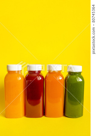 Fresh juices or smoothies of fruits and vegetables in bottles on a yellow background.  80745364