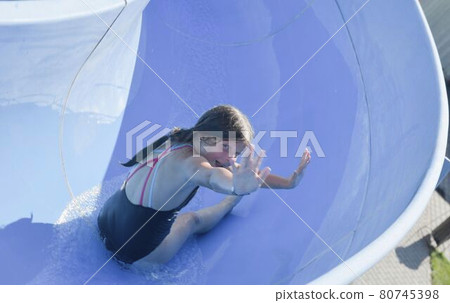 Happy kid on water slide at water park. Water slide with flowing splash water at aqua park. Summer aqua park holiday. Vacation concept Happy kid on water slide at water park. Water slide with flowing splash water at aqua park. Summer aqua park holiday. Vacation concept 80745398
