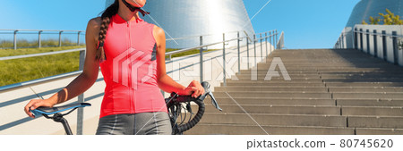 Road cycling in city cyclist athlete woman with bike wearing pink jersey outfit for sports biking on summer urban commute ride. Bicycle concept panoramic background Road cycling in city cyclist athlete woman with bike wearing pink jersey outfit for sports biking on summer urban commute ride. Bicycle concept panoramic background 80745620