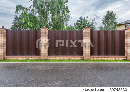 Brown metal fence along the road after rain. 80748880