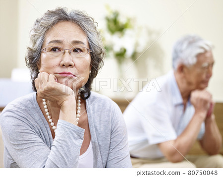 senior asian couple sitting on couch at home, angry at each other 80750048