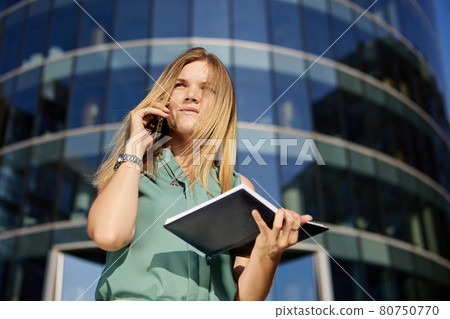 Business woman makes an appointment by phone outdoors on the go. Business woman makes an appointment by phone outdoors on the go. 80750770