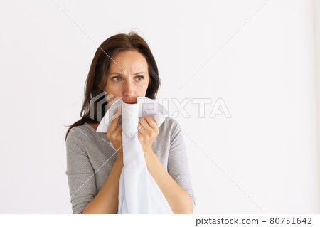 Woman sniffing clean shirt on light background Woman sniffing clean shirt on light background 80751642