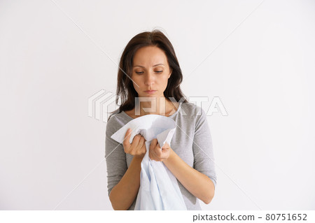 Woman sniffing clean shirt on light background Woman sniffing clean shirt on light background 80751652