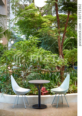 Empty tables and chairs in a cafe with lots of trees and plants 80751902