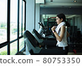 Side view of beautiful girl running on treadmill at gym 80753350