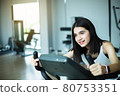 Fit young girl using exercise bike at the gym. Fitness female using air bike at gym. 80753351