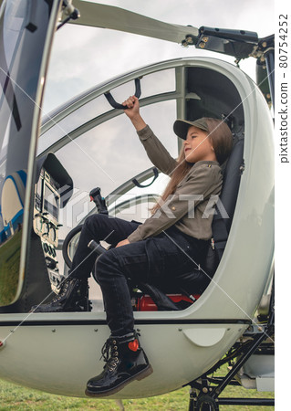 Smiling preteen girl sitting on pilot seat in open helicopter cockpit 80754252