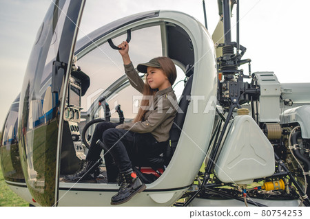 Tween girl sitting on pilot seat in modern helicopter cockpit 80754253