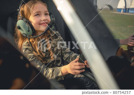 Smiling preteen girl in aviator headset sitting in helicopter cockpit 80754257