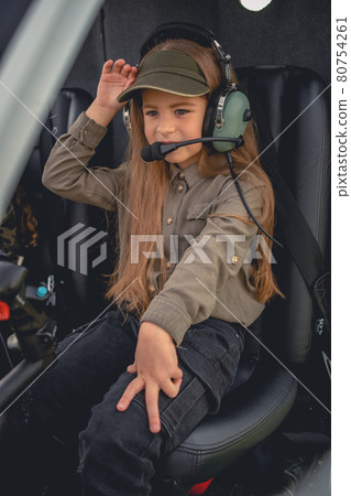 Interested preteen girl in headset sitting on pilot seat in helicopter Interested preteen girl in headset sitting on pilot seat in helicopter 80754261