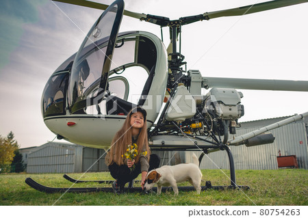 Cheerful preteen girl playing with puppy near helicopter Cheerful preteen girl playing with puppy near helicopter 80754263