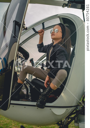 Smiling tween girl in mirrored sunglasses looking at sky from helicopter cockpit 80754281