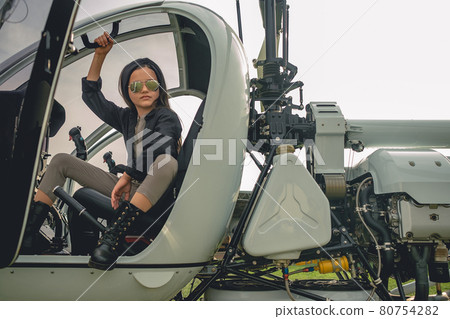Brunette tweenager in mirrored sunglasses sitting in open helicopter cockpit 80754282