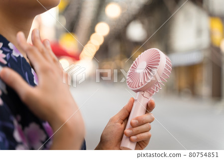 A woman in a yukata cooling off with a mini electric fan (handy fan) in the evening shopping district at Endoji Shopping District 80754851