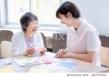 Nursing image: Senior woman folding origami and a caregiver Photo cooperation: Japanese language school attached to Chuo Institute of Technology 80754916