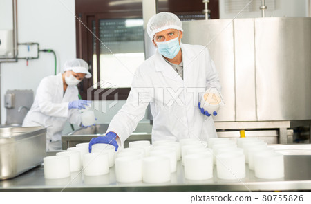 Cheesemaker in protective mask working in shaping workshop of cheese factory Cheesemaker in protective mask working in shaping workshop of cheese factory 80755826
