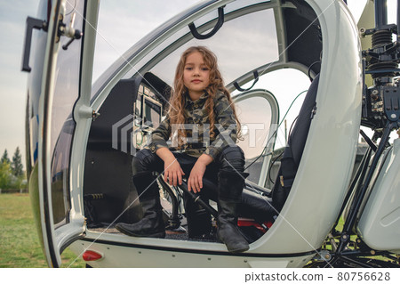 Confident preteen girl in camo style blouse sitting in open helicopter Confident preteen girl in camo style blouse sitting in open helicopter 80756628